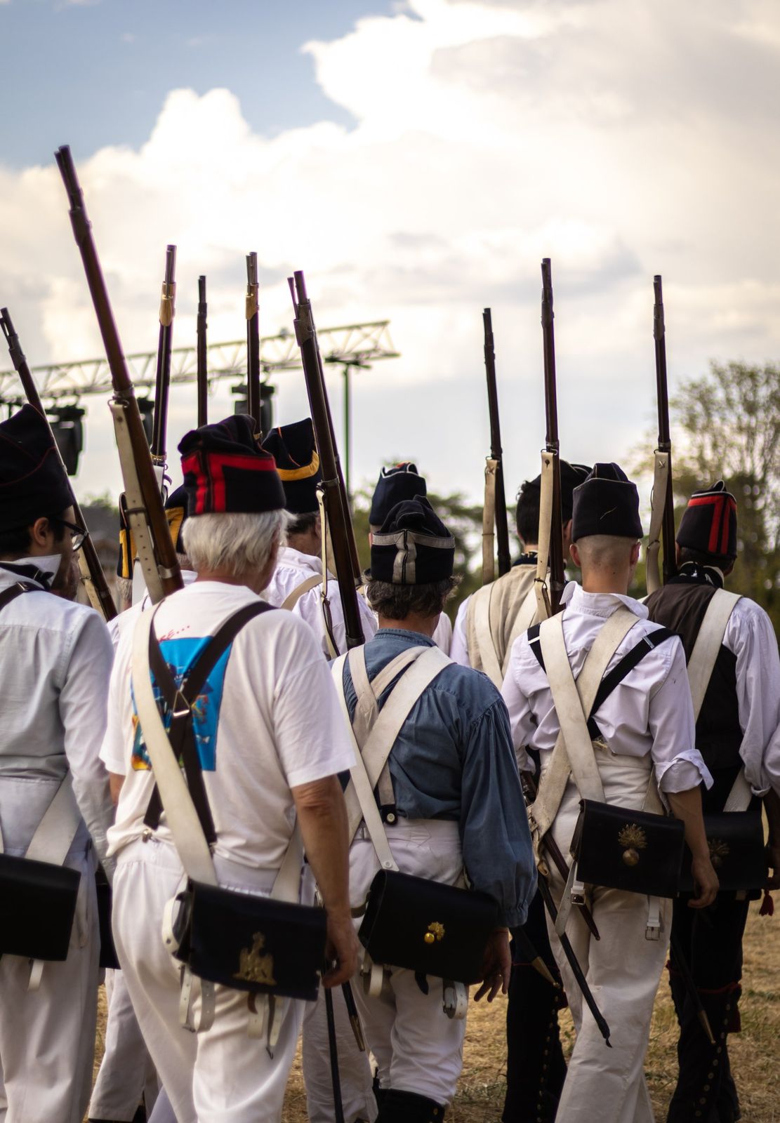 Des fantassins en uniforme blanc et bonnet de police, fusil à l’épaule, vus de dos