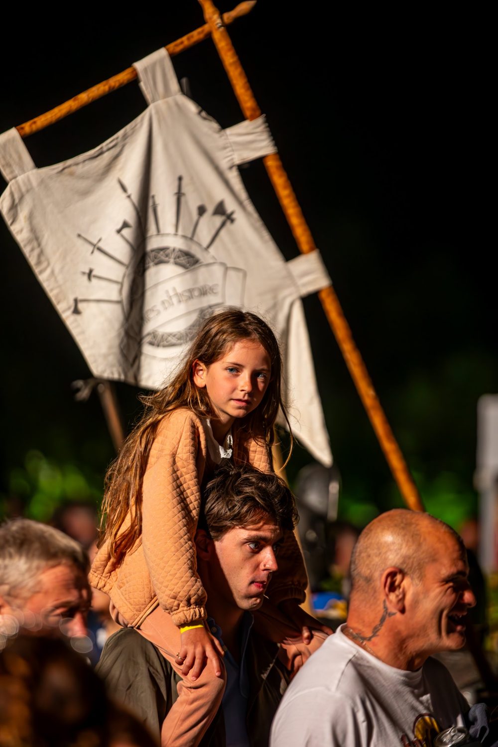 Une petite fille sur les épaules d’un spectateur, devant une bannière d’histoire