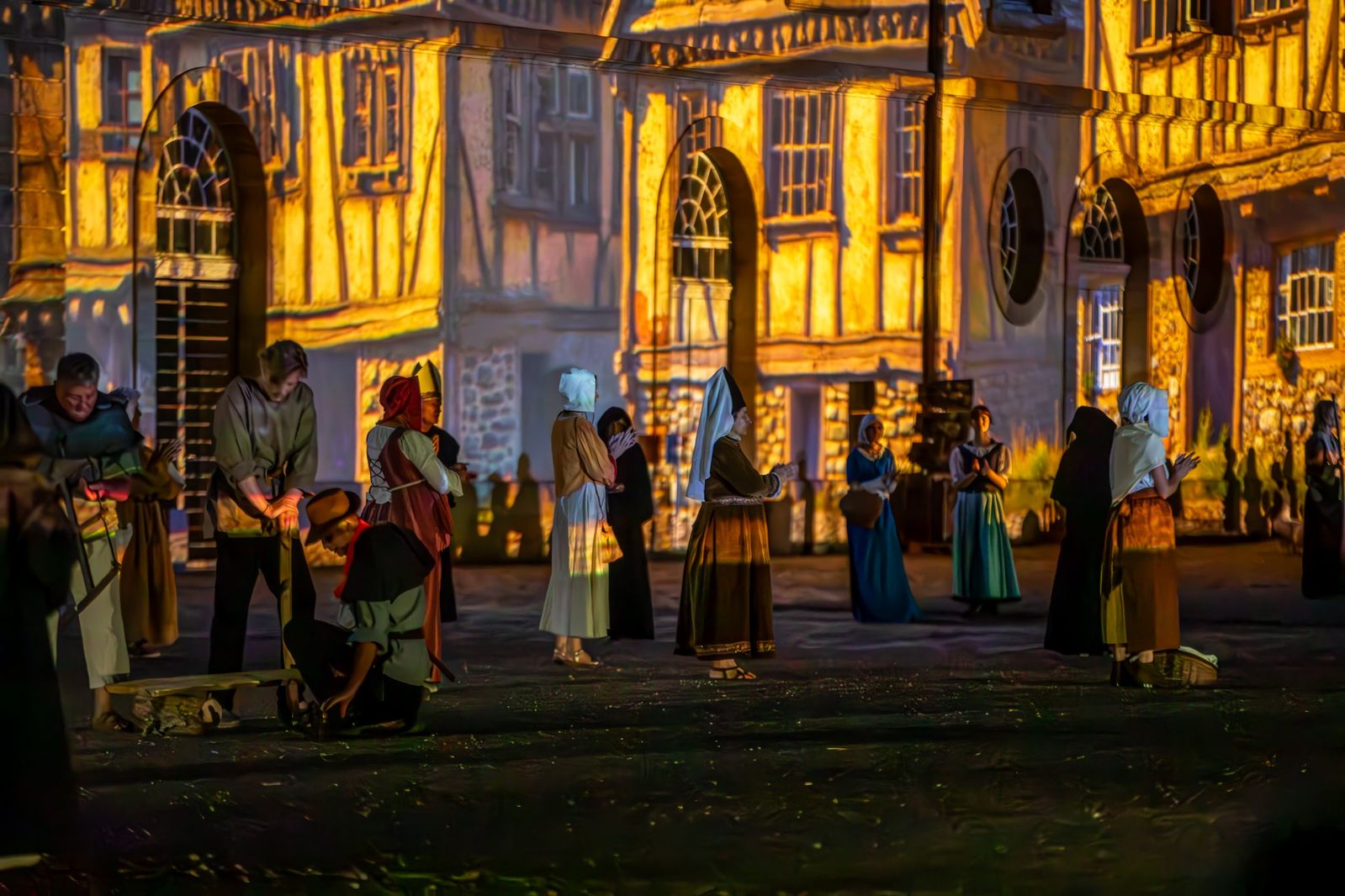 Des villageois en costume médiéval devant des maisons à colombages éclairées